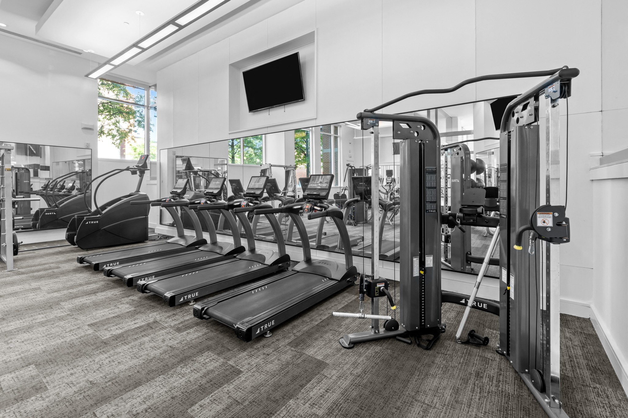a gym with cardio equipment and a tv on the wall